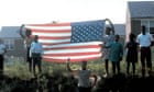 People hold aloft a large American flag as Robert Kennedy's funeral train passes by in 1968