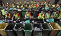 Volunteers in fluorescent jackets stand behind wheelie bins sorting waste at Glastonbury festival 