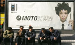 Men sit on the sidewalk in front of a Motorola advertising billboard in Beiijng, China