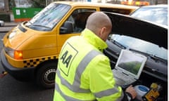 An AA patrolman studies a laptop under the open bonnet of a car, with his van parked beside it