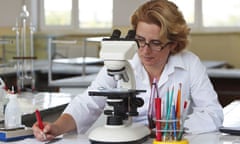 Female researcher taking notes while she is using a microscope