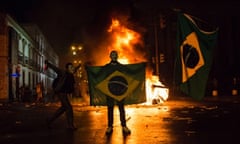 Brazil Protest: A demonstrator holds a Brazilian flag in front of a burning barricade. Protesters massed in at least seven Brazilian cities overnight