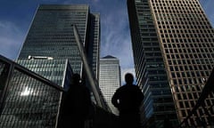 Silhouetted workers walk in front of office towers in the Canary Wharf financial district in London