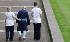 Two NHS staff walk with an elderly patient 