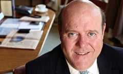 A smiling Rupert Soames in suit and tie with his office in the background