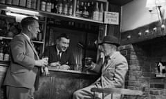 An image from 1962 of a man in a hat drinking by a pub fireplace