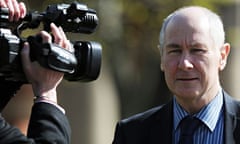 John Darwin in dark suit and tie puts up with a news camera directed on him as he leaves court