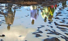 Sudanese are reflected in a pool of rain water in southern Sudan