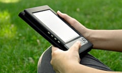 Young woman reads electronic book sitting on the grass. Shallow depth of field.