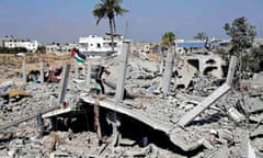 A Palestinian flag flutters as a man searches the remains of his house