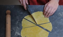 an overhead view of a lady cutting triangles of pasta from a solid sheet she has made herself