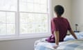 Teenage boy (16-18) sitting on bed, looking out window, rear view