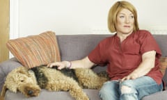 Kellie Maloney in jeans and a shirt sitting on a sofa with her hand on a sleeping curly-haired dog 