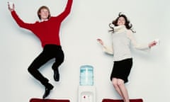 A man and a woman jumping on office chairs