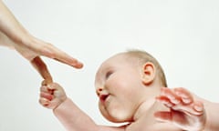 A young baby holds an adult's hand