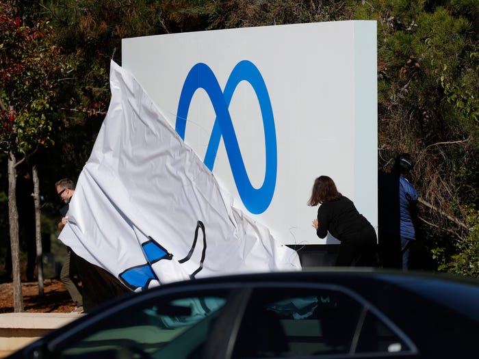 Workers in front of Facebook headquarters pull off cover of the old "thumbs up" sign to reveal the new Meta logo