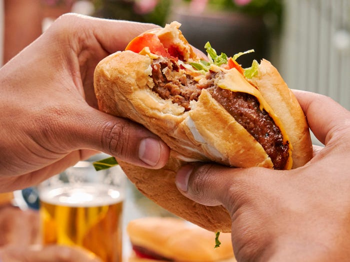 Hands holding a Beyond Burger with a bite taken out of it.