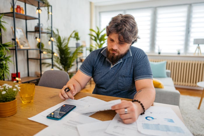 Photo of a young man sitting at the kitchen table working on his taxes at home.