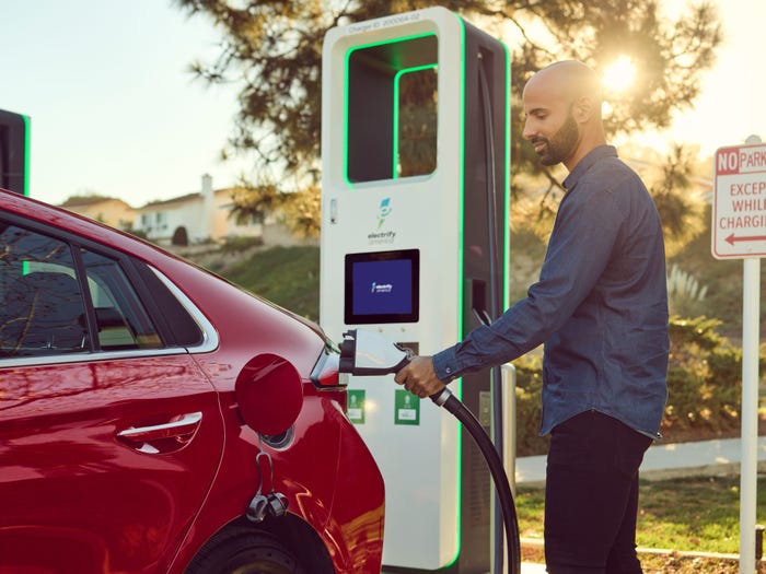 A man plugs an EV charger into a red electric car.