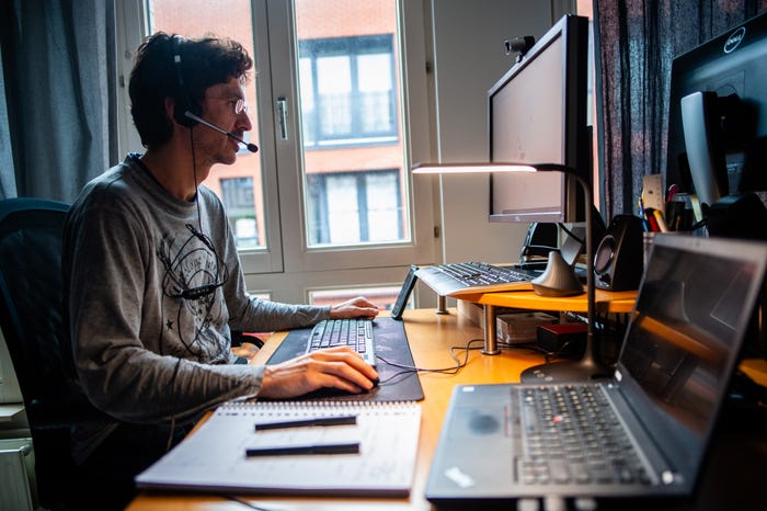 A man sits at a desk wearing a headset, facing a computer screen.