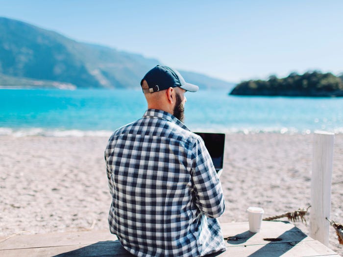 A man sitting on a beach with a laptop.