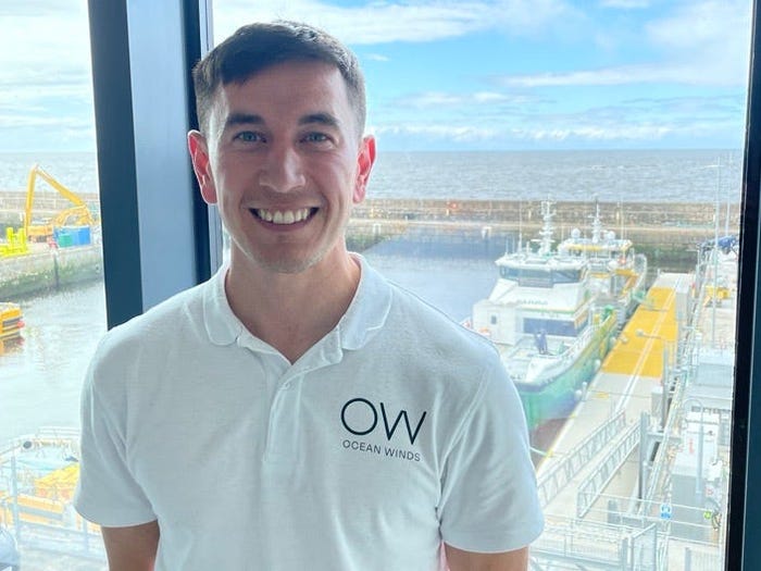 Shaun Mitchell, a supervisor at the offshore wind company Ocean Winds, poses in front of window overlooking a sea vessel.