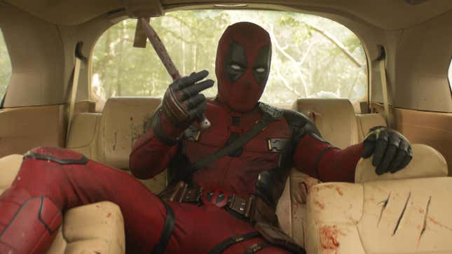 Deadpool gestures with a stick in his hand in the back seat of a busted car.