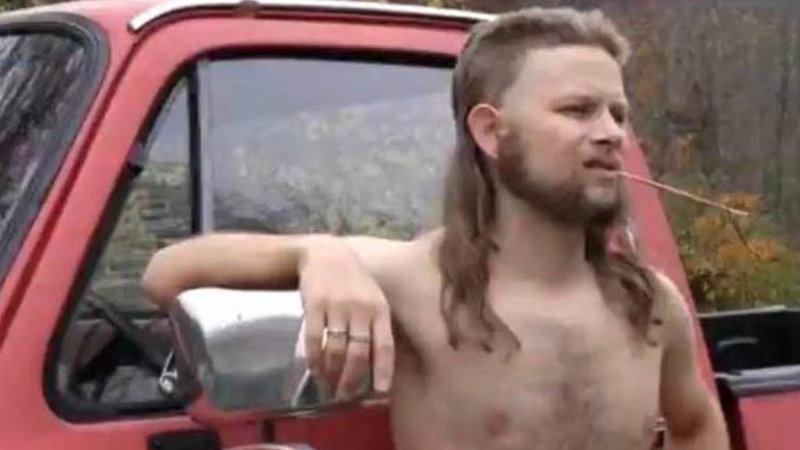 zach downey shirtless with a mullet leaning on a red pickup truck