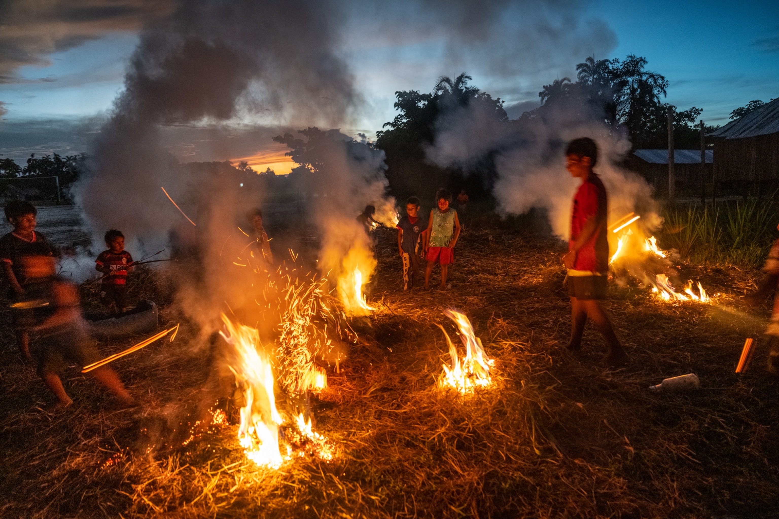 Burning dry grass and children adding more fuel to the fires at sunset.