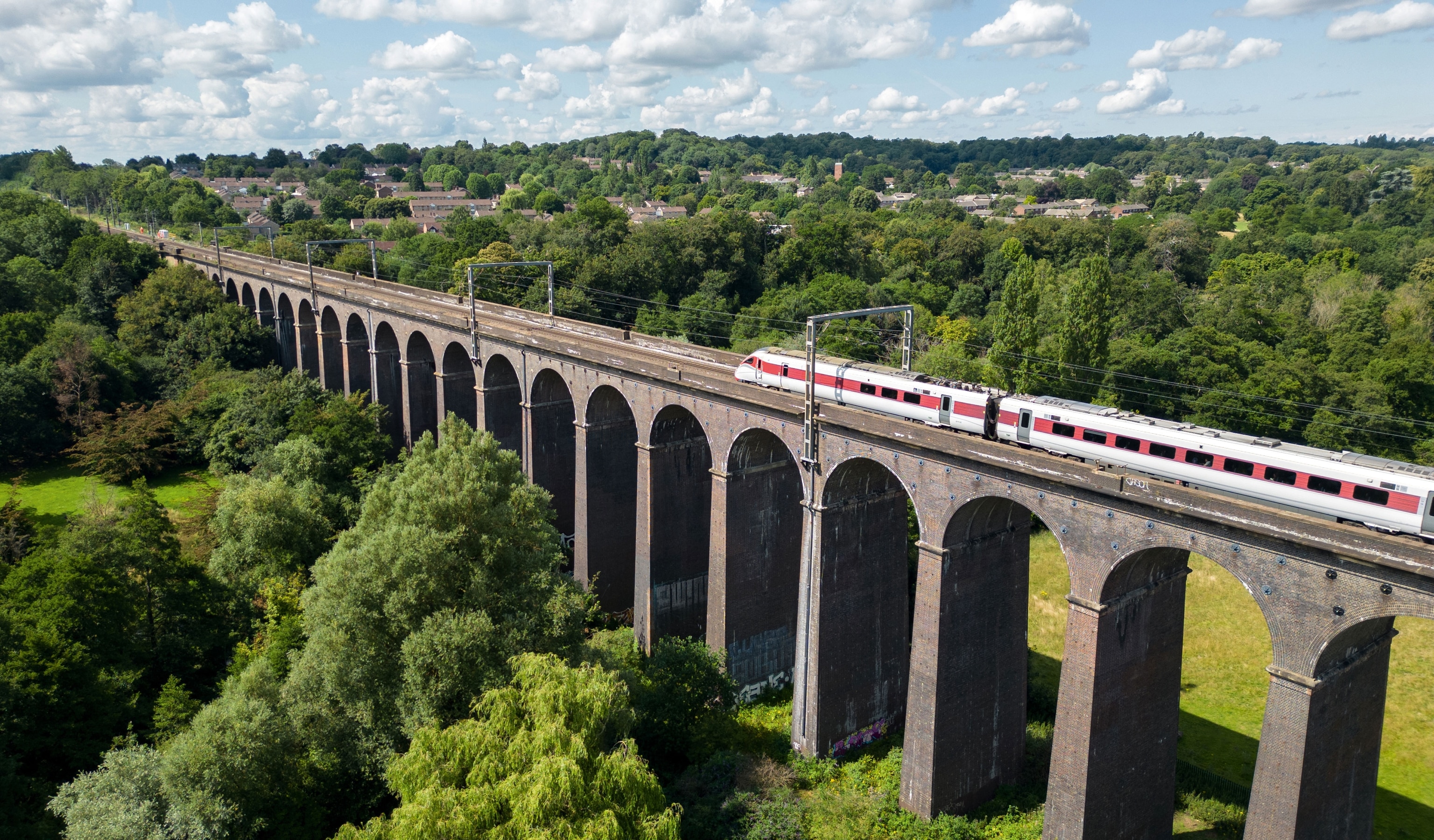 Aerial view of a high speed train travelling over bridge surrounded by greenery