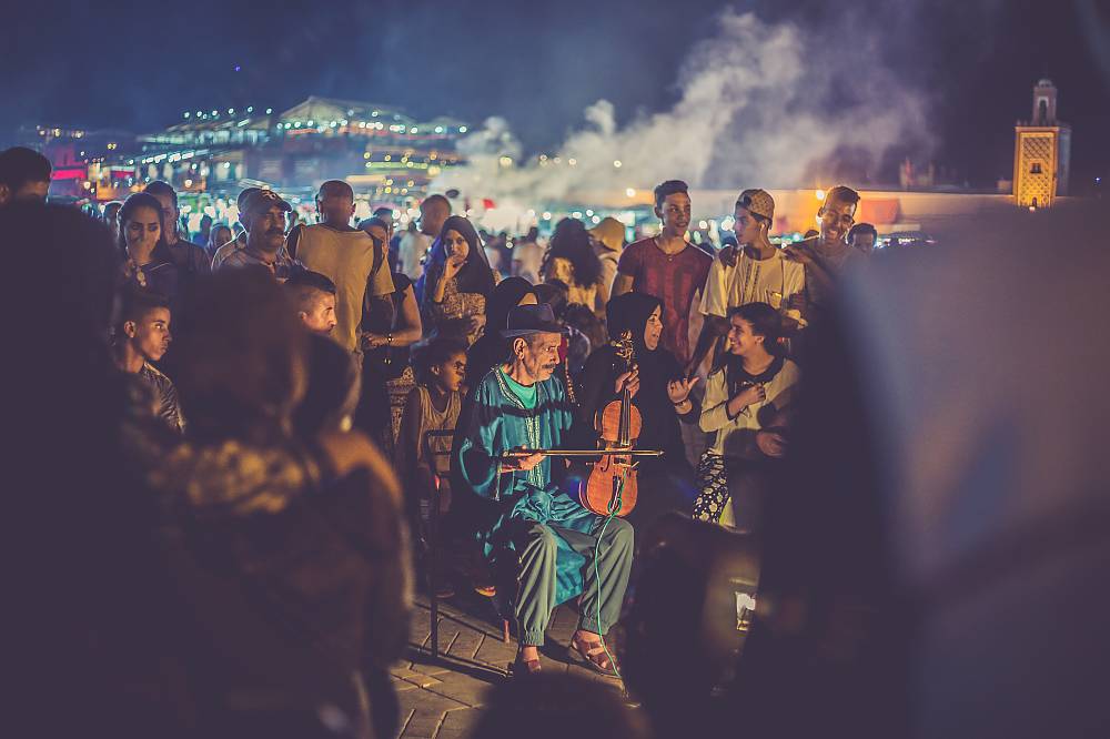 Violin player at Jemaa el-Fna Square with crowd of people and smog of the market