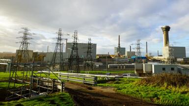 Pylons, wires and fences are seen with grass in the foreground and a cloudy but blue sky, at the Sellafield nuclear site in Seascale in 2016.