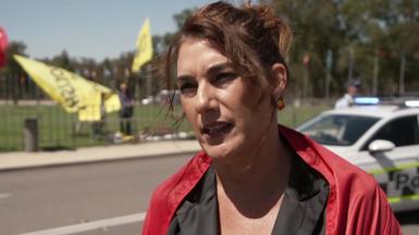 A woman speaking with protestors and a police car in the background