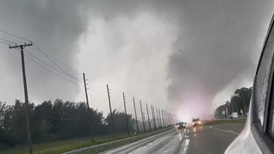 A picture of a tornado at the end of a road, with cars on it, and a white flash inside it