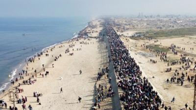 Thousands of people walk along a road near the beach and sea in Gaza