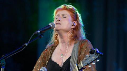 Eddi Reader, a red-haired female singer with a guitar, has her eyes closed as she performs in front of a microphone