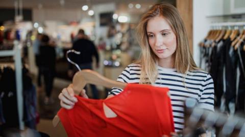 Woman wearing a stripy top shopping and looking at red top on a hanger