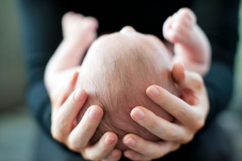 A baby lies in a pair of arms with hands supporting its head