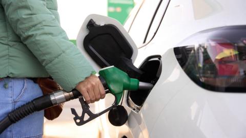 A person wearing a light green jacket filling up their car with petrol