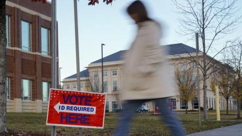 A blurry image of a person walking past a sign saying VOTE HERE - ID required.