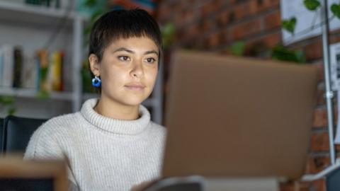 A woman sits at a computer at home