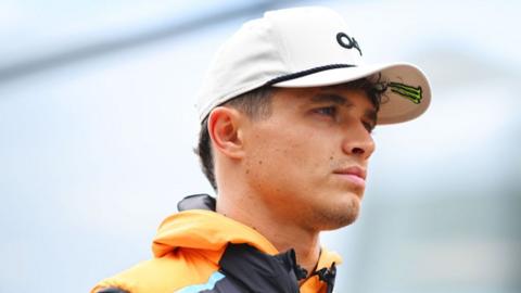 Lando Norris looks on sternly while wearing a cap