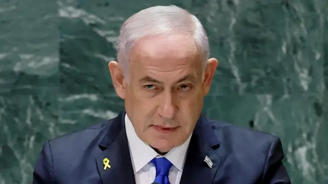 Benjamin Netanyahu in blue suit and tie with pin of israel flag on lapel and green background