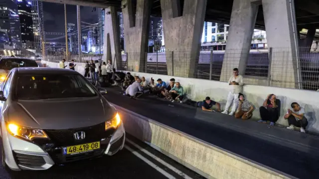 People take cover behind vehicles under a bridge along the side of a highway in Tel Aviv last night