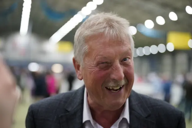 Man with white hair and white moustache smiling