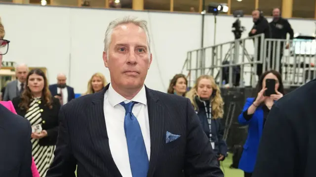 Man with white hair in pinstripe suit and blue tie