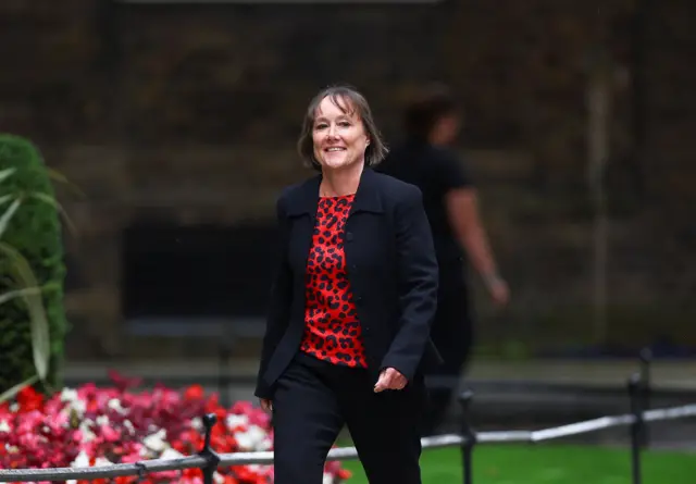 A woman with short brown hair wearing a red blouse with a black blazer