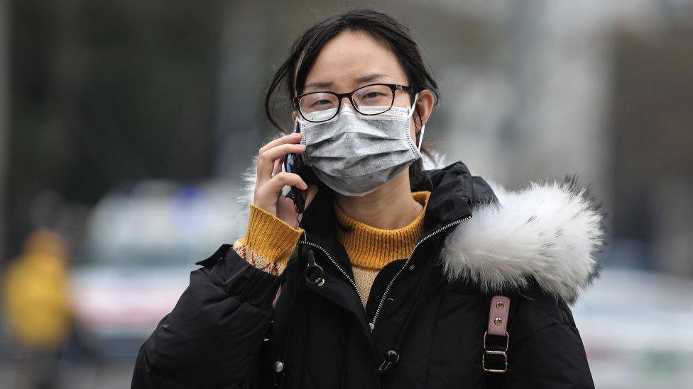 A woman wears a mask while walking past the closed Huanan Seafood Wholesale Market, which has been linked to cases of Coronavirus, in Wuhan