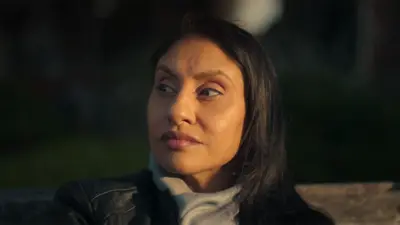 Still from the Netflix documentary with Kirat, a woman, looking to the left while sitting outside. She is wearing a black leather jacket and grey scarf.