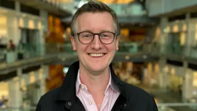 Alex Green smiling with offices behind him